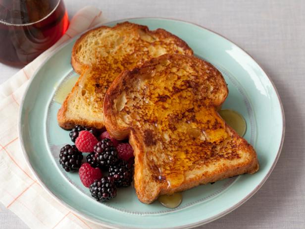 French Toast covered with syrup alongside a serving of raspberries and blackberries on a pale blue plate