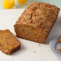 A loaf of Brown Pumpkin Bread with one slice removed that is placed on a plain white surface