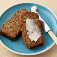 Two slices of Banana Bread, one of which contains spread butter, on a small blue plate with white edging