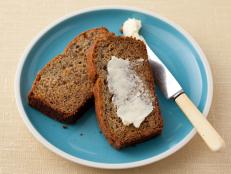 Two slices of Banana Bread, one of which contains spread butter, on a small blue plate with white edging