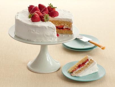Strawberry Shortcake topped with strawberries that is placed on a white cake pedestal near a removed slice of cake