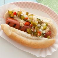 A grilled hot dog with pickle relish on a bun placed on a white plate with red grid-like edging