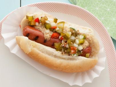 A grilled hot dog with pickle relish on a bun placed on a white plate with red grid-like edging