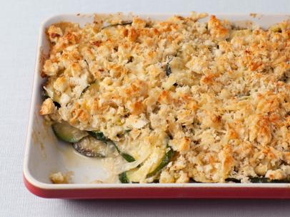 A zucchini gratin in a red and white baking dish placed on a textured white table setting