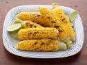 Six ears of grilled corn with pieces of lime on a white and blue dish