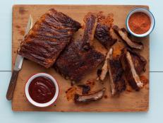 Pieces of beef and pork ribs with sauce, spices and a knife placed on a wooden cutting board