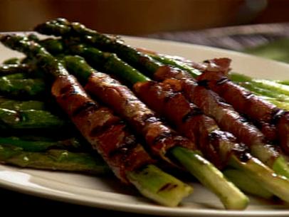 Several pieces of grilled asparagus wrapped in ham on a plain white plate