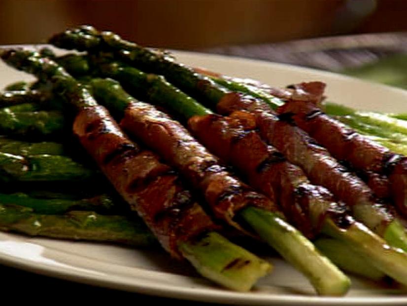 Several pieces of grilled asparagus wrapped in ham on a plain white plate
