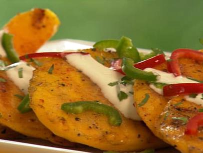 Pieces of grilled mango topped with crema, chopped green and red peppers against a green background
