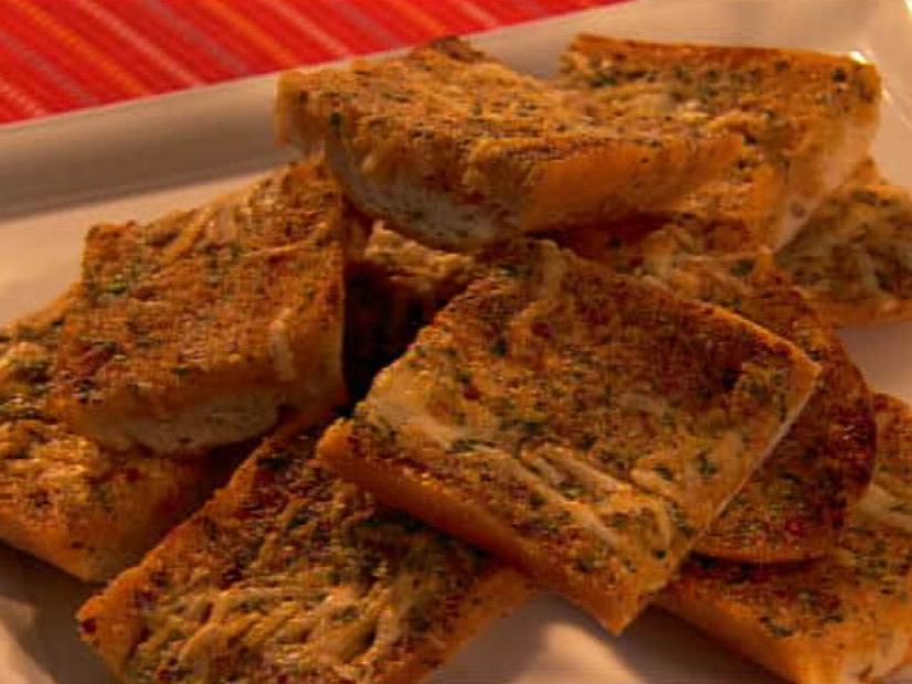Pieces of garlic bread topped with herbs and cheese piled on a white platter