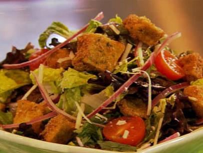 A mixed salad containing eggplant, tomatoes and croutons in a white dish