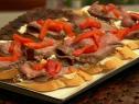 Flank steak topped with red peppers on pieces of bread on a white plate with black trim