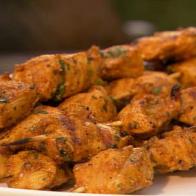 Several pieces of curry chicken on skewers placed on a white dish