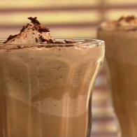 A coffee frappe topped with chocolate shavings in a tall slender glass