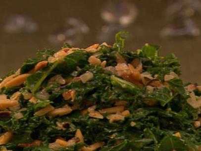 A close-up of a pile of kale and toasted almonds against a dark hazy background