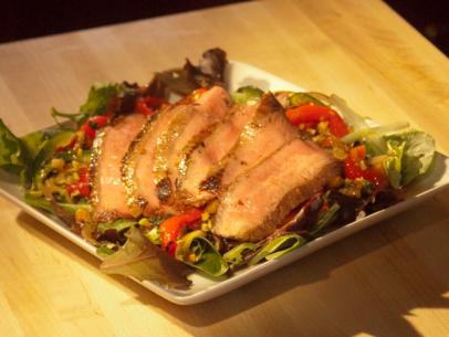 Slices of beef on a bed of lettuce and tomatoes that lie on a square white plate