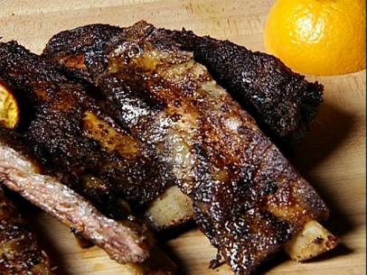 Pieces of smoked beef ribs on a wooden surface next to a half of a lemon