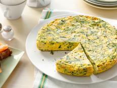 A round egg and herb dish with a slice removed that is placed on a simple round white plate