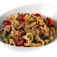 Campanelle pasta mixed with tomatoes, tuna, capers and artichoke hearts in a simple white boat shaped bowl