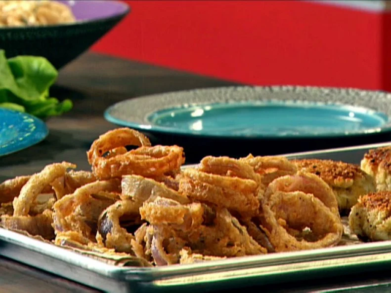 Season coated onions rings on a baking sheet thats placed on a counter with a blue plate with crackled edging