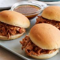 Three pulled pork sandwiches aligned on a white platter in front of light pink flowers