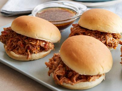 Three pulled pork sandwiches aligned on a white platter in front of light pink flowers