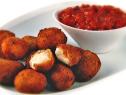 A pile of Bocconcini and a dish of Tomato And Garlic Chutney that are placed on a white simple oval dish
