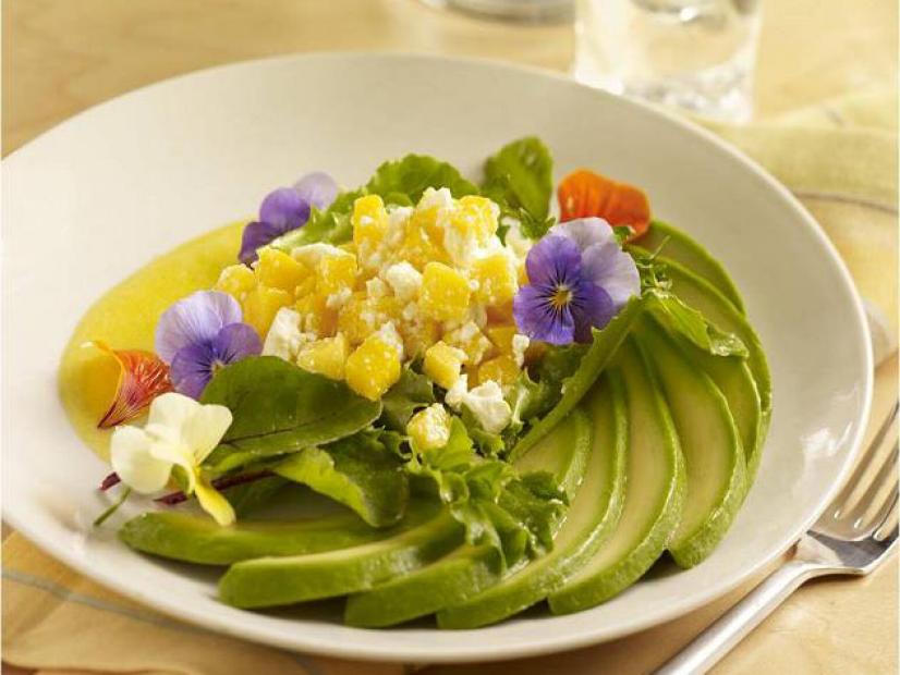 A fan of avocado slices accompanied with mango salad and decorated with red, purple and white flowers
