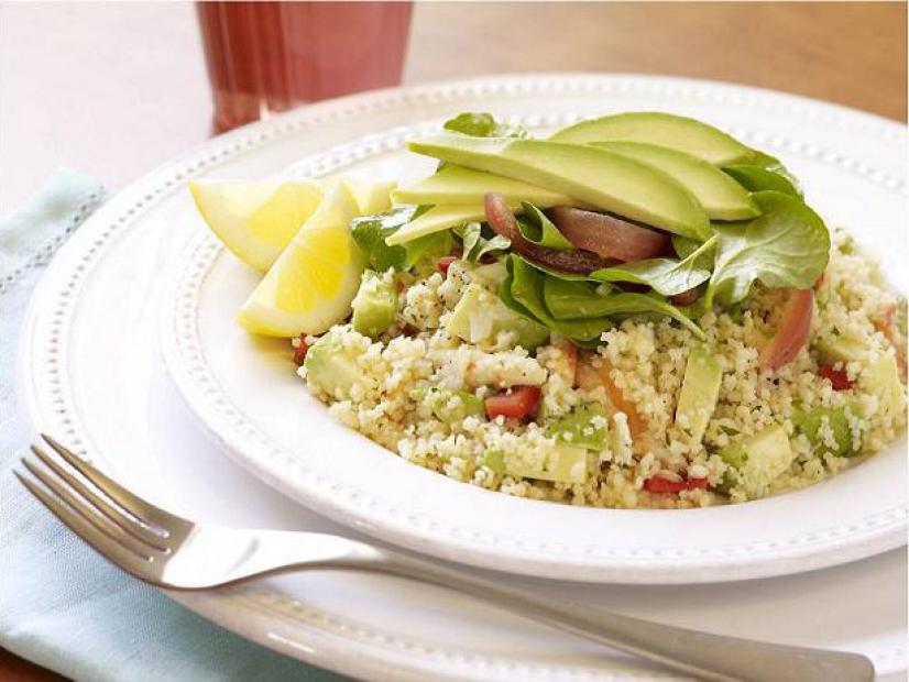 A couscous salad mixed and topped with avocado and two lemon wedges on simple white dishware with beaded edging