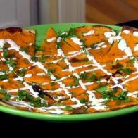 A green plate containing tortilla chips covered with melted cheese, sour cream and chopped cilantro