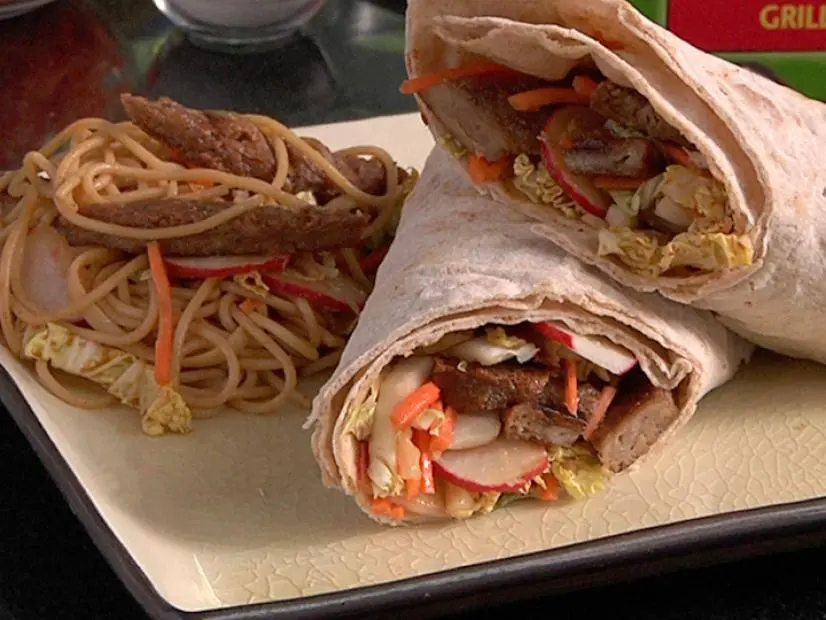Two halves of a wrap beside a portion of the wrap ingredients on a small square cream colored plate
