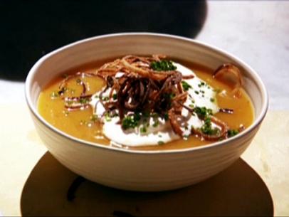 Butternut squash soup topped with cinnamon whipped cream and fried shallots in a simple white bowl with ridges