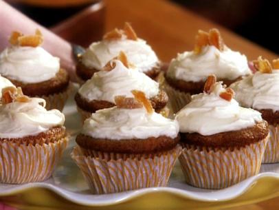 Small cupcakes topped with white icing and crystallized ginger on a white platter with scalloped edges