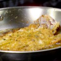 Pan fried trout covered with bread crumbs, fresh herbs, and red pepper flakes cooks in a skillet.
