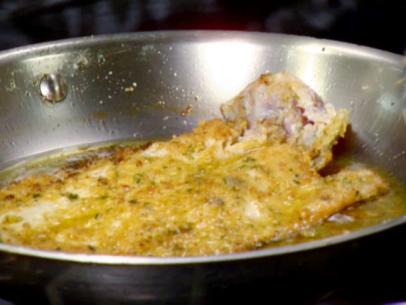 Pan fried trout covered with bread crumbs, fresh herbs, and red pepper flakes cooks in a skillet.