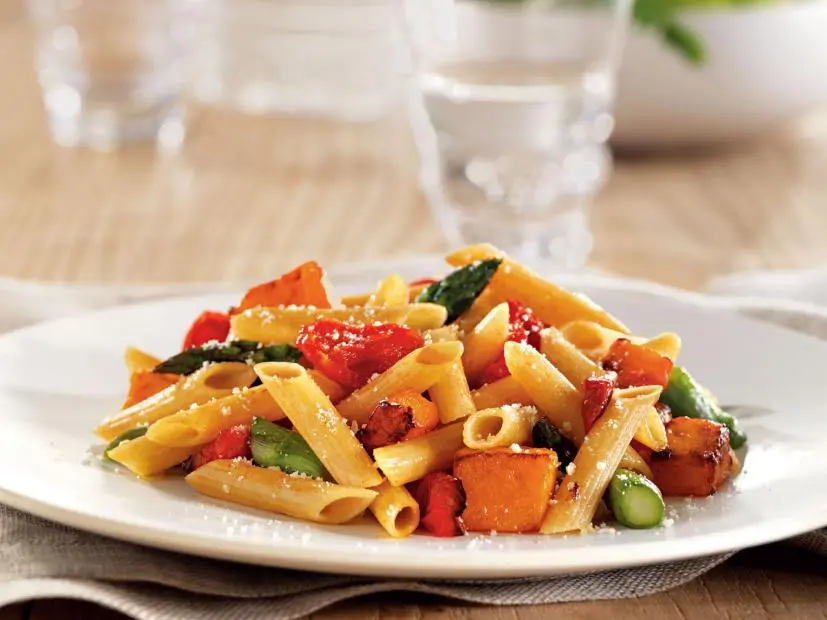 Penne pasta mixed with asparagus, red peppers and parmesan cheese on a simple white plate