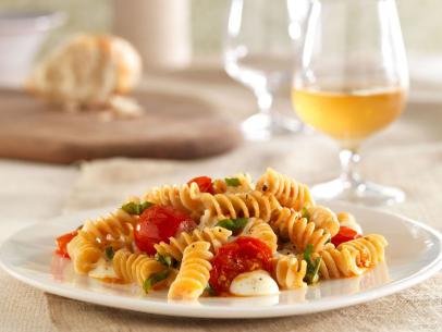 Rotini mixed with tomatoes, basil and mozzarella on a simple white plate next to a glass of white wine