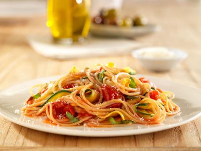 Spaghetti mixed with squash, parmesan cheese, tomatoes and zucchini on a simple white plate