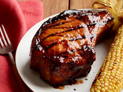 A piece of barbecued pork alongside an ear of corn on a simple white plate