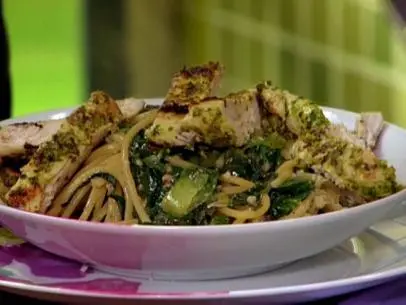 Chopped chicken mixed with pesto and arugula leaves on a bed of caesar salad atop spaghetti