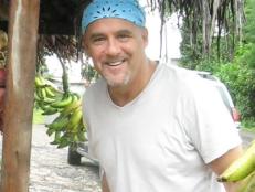 Former Season 6 Next Food Network Star Michael Salmon standing next to a fruit stand while wearing a white t-shirt and a light blue bandana
