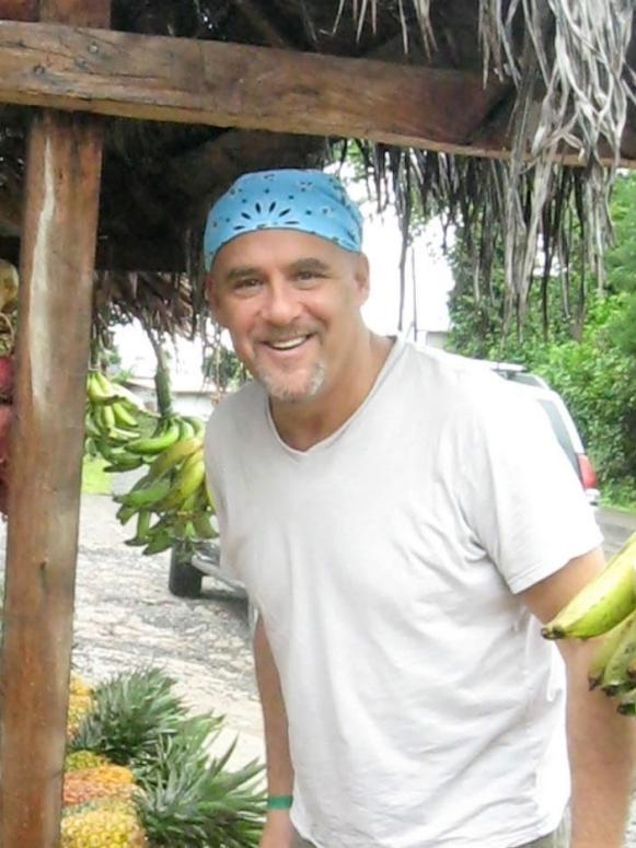 Former Season 6 Next Food Network Star Michael Salmon standing next to a fruit stand while wearing a white t-shirt and a light blue bandana