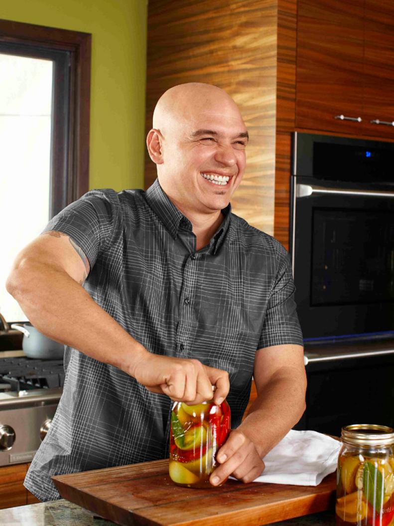 Michael Symon smiling as he twists a lid on a jar of sliced tomatoes