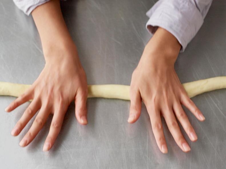 A cavatelli how-to displaying two hands rolling out dough on a stainless steel countertop