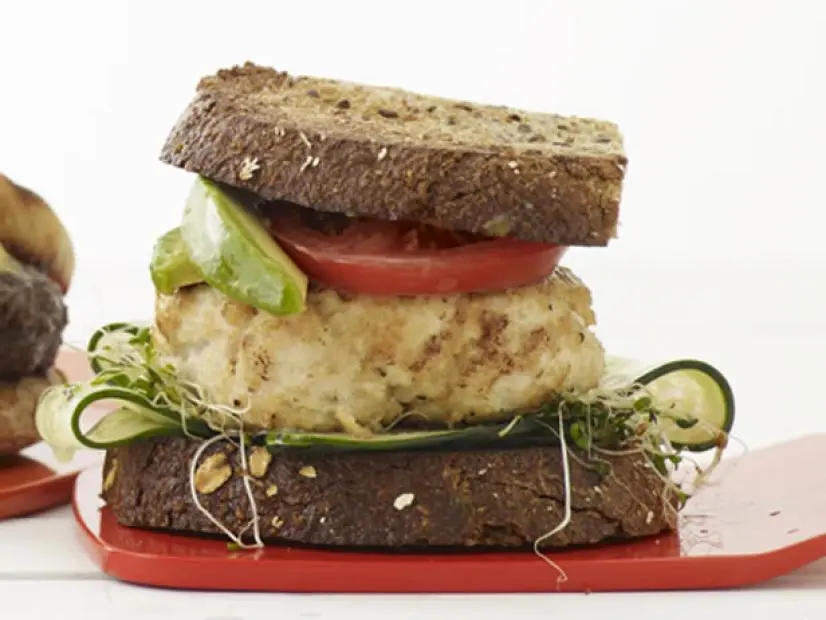 A sandwich made with an unidentifiable meat and accompanied by tomatoes, apples and sprouts