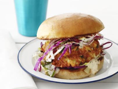 A sandwhich made of chicken topped with coleslaw on a small white plate with dark blue edging