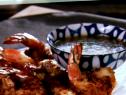 A close up of a white platter with ginger and coconut crusted jumbo shrimp. The jumbo shrimp were battered and fried in peanut oil. Beside the shrimp is a blue and white patterned bowl with a sweet mango lime dipping sauce for the shrimp.