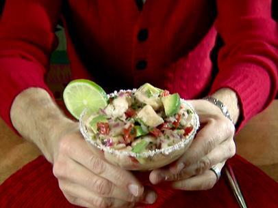 Hands hold a salt rimmed margarita glass that has been filled with ceviche made from catfish cubes that were marinated with citrus juices and zests. The fish was combined with a salad of seeded and minced jalapeno, diced red onion, seeded and diced tomato, sliced garlic, chopped fresh cilantro, chopped fresh oregano, and a diced avocado.