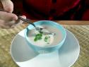 A hand places a spoon into a small bowl with Asian soup. This soup was made with ingredients such as fish stock, lemongrass, galangal or blue ginger, seeded and sliced habanero, cilantro leaves, fish sauce, lime juice, cubed catfish filets, and coconut milk.