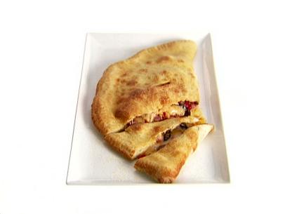 An antipasto calzone that has been cut into slices and served on a white rectangular platter. This pizza dough was stuffed with salami, roasted red peppers, olives, and cheese.